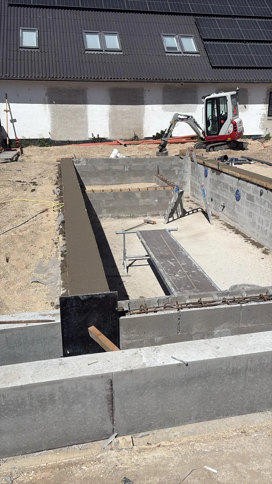 Betonkonstruktion til en pool under udførelse foran en bolig.